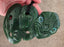 Green jade pendant with intricate carvings held in a hand on a beige surface
