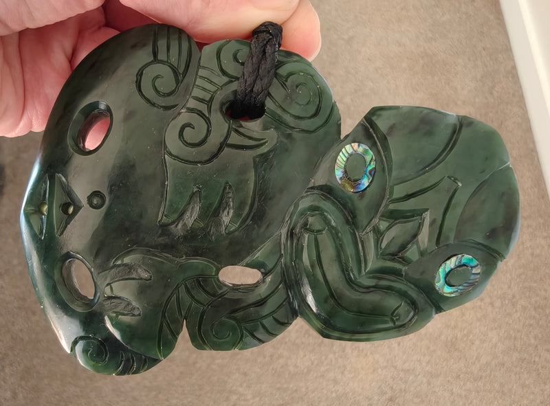 Green jade pendant with intricate carvings held by a hand on a beige background