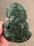 Green jade pendant with intricate carvings held by a hand on a beige background