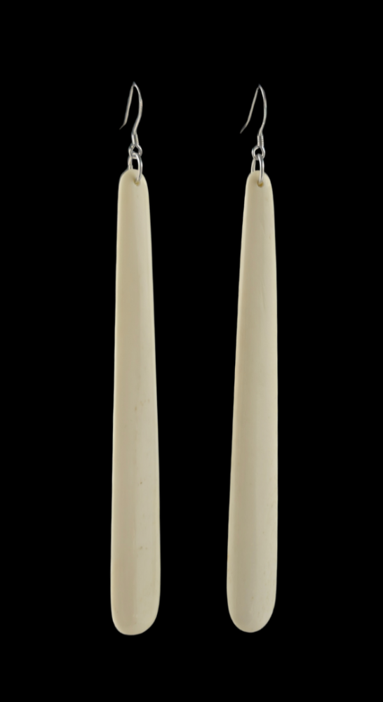 Pair of long, thin, off-white earrings on a black background