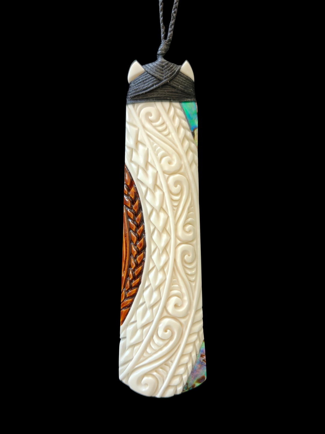 A carved whale bone pendant with intricate Celtic swirl patterns, a brown braided design, and a dark gray wrap at the top, hanging against a solid black background.