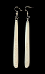A pair of long, narrow white carved dangle earrings with silver fishhook wires, shown against a solid black background.