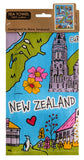 A rectangular tea towel featuring a colorful illustrated New Zealand map and landmarks, hanging from a brown cardboard hanger. The design includes blue water, green land, pink and yellow flowers, a gray tower, and the words 'NEW ZEALAND' across the center.