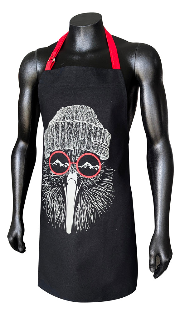A black apron with red neck straps displayed on a black mannequin torso. The apron features a graphic illustration of a bird's face wearing a gray knit beanie and red-rimmed sunglasses with mountain silhouettes.