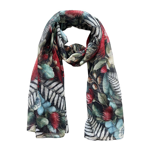 A lightweight scarf with a dense tropical leaf and floral print in red, green, blue, and black and white, draped against a solid white background.