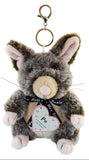 A plush toy rabbit keychain with a metal clasp and ring, featuring gray and brown fur, pink inner ears and paws, a cream snout, and a black ribbon with a heart-shaped tag that reads 'Po' and 'New Zealand'.