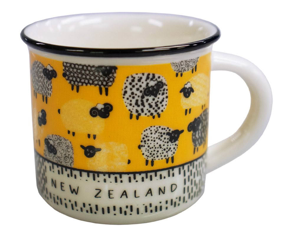 A white enamel mug with a yellow band around the middle featuring black and white sheep illustrations and the words 'NEW ZEALAND' printed on a patterned section near the base.