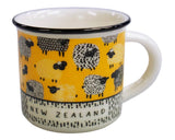 A white enamel mug with a yellow band around the middle featuring black and white sheep illustrations and the words 'NEW ZEALAND' printed on a patterned section near the base.