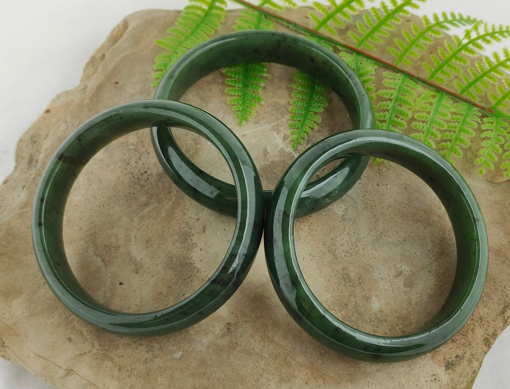 Three green jade bangle bracelets displayed on a textured surface with a background of fern leaves. Main image