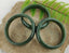Three green jade bangle bracelets displayed on a textured surface with a background of fern leaves.