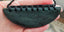 A greenstone breast plate pendant with a black adjustable slipknot cord, held between fingers.