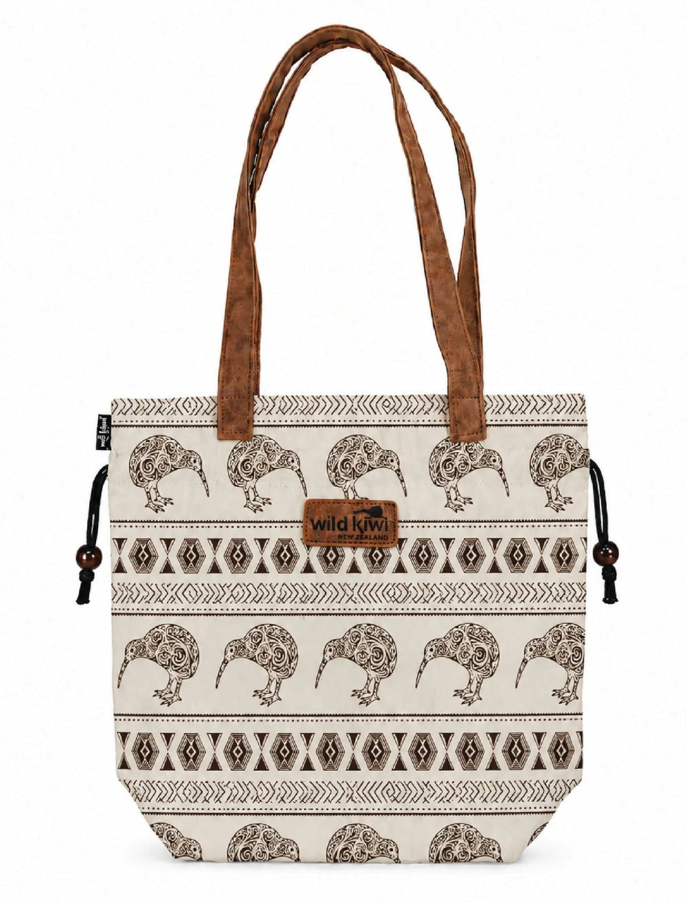 A tote bag with a cream canvas body featuring a brown kiwi bird and geometric tribal pattern, brown faux-leather handles, and a brown leather patch with the 'wild kiwi' logo. Main image