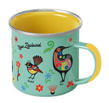 A mint green enamel camping mug with a yellow interior and handle, decorated with colorful New Zealand bird and floral motifs, and the words 'New Zealand' 
