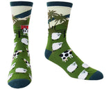 A pair of crew socks with a green farm landscape print, featuring sheep, cows, palm trees, and a dark green cuff and toe, displayed against a plain white background.