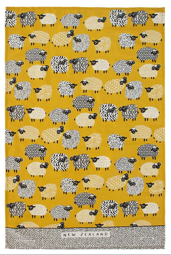 A woven tea towel featuring a repeating pattern of stylized sheep in black, white, and beige on a mustard yellow background, with a textured gray border at the bottom containing the text 'NEW ZEALAND'. Main image