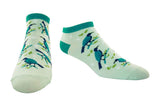 A pair of low-cut socks with a light mint green background, featuring a pattern of blue and dark tui birds perched on branches with green leaves. The socks have solid teal cuffs, heels, and toes, and are displayed against a plain white background.