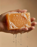 Hand holding a bar of Wild Ferns soap with a beige background