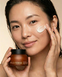 Woman applying cream to her face with a jar of Wild Ferns product in front of her.