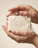 Hand holding a bar of soap with 'Wild Ferns' branding against a neutral background