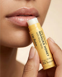 Lip balm stick with 'Manuka Honey' label held by a hand near lips