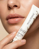 Hand holding a tube of Wild Ferns lip care product near lips