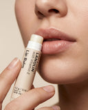 Person applying a Lanolips lip balm to their lips with a beige background