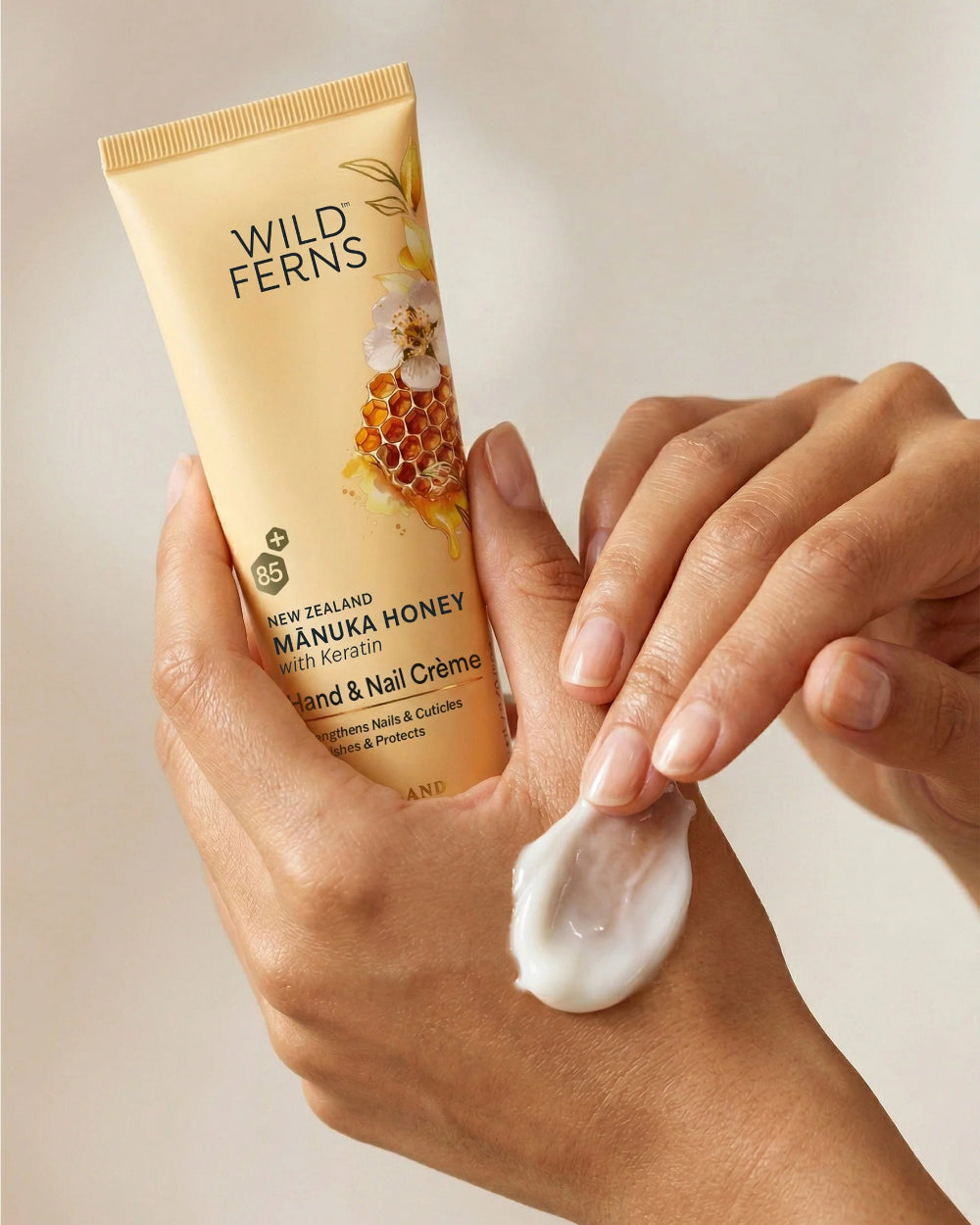 Hand applying Wild Ferns Manuka Honey Hand & Nail Crème to a hand with a beige background