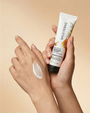 Hand holding a tube of Wild Ferns hand cream with a swatch on skin against a beige background