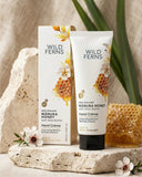 Wild Ferns Manuka Honey hand cream and packaging on a stone surface with honeycomb and flowers.