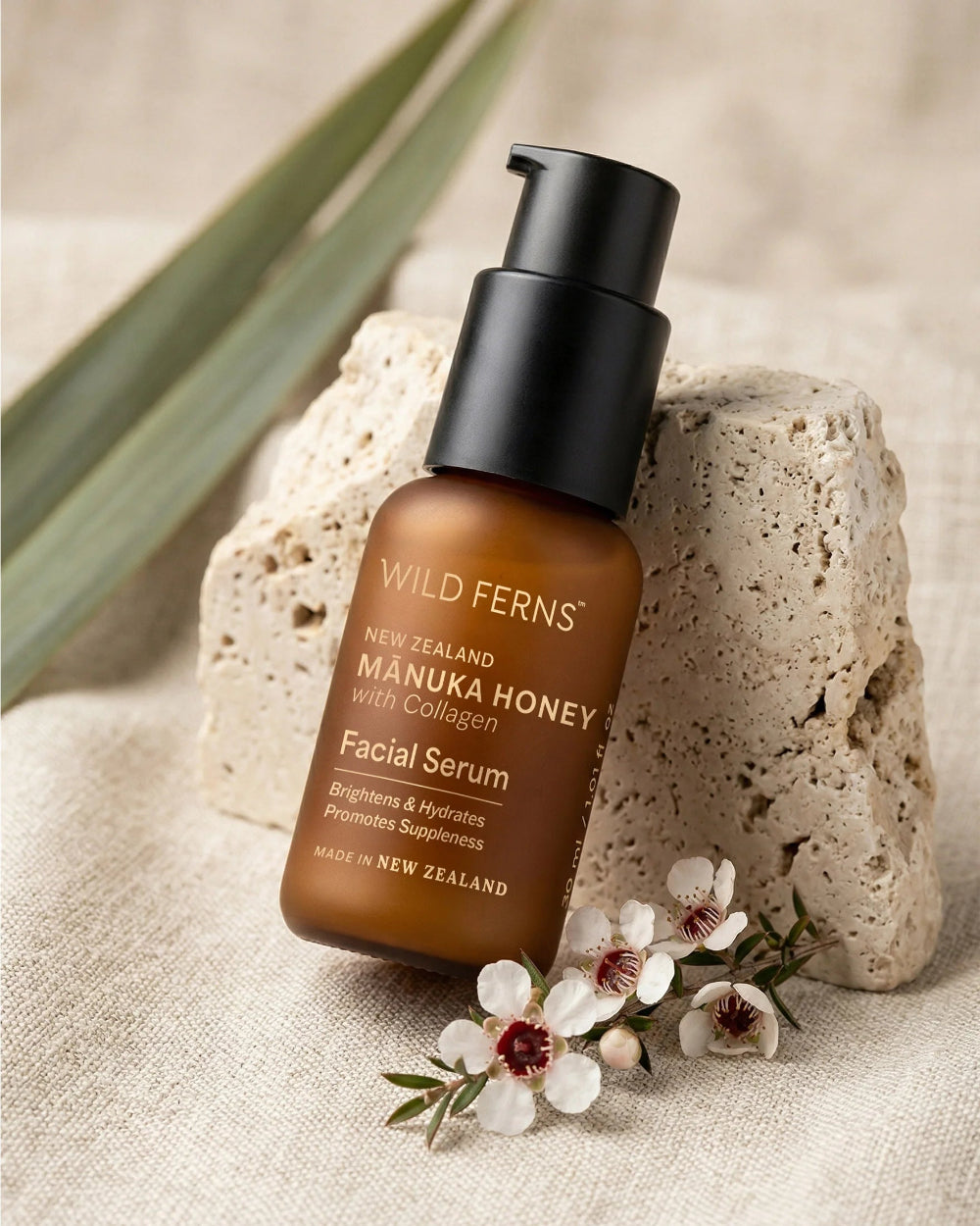 Wild Ferns Manuka Honey Facial Serum bottle on a stone surface with flowers and leaves.