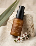 Wild Ferns Manuka Honey Facial Serum bottle on a stone surface with flowers and leaves.