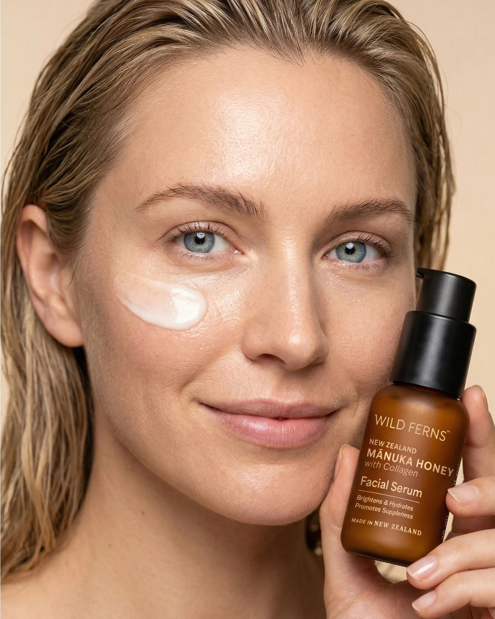 Woman holding a bottle of Wild Ferns facial serum with product on her face.