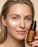 Woman holding a bottle of Wild Ferns facial serum with product on her face.