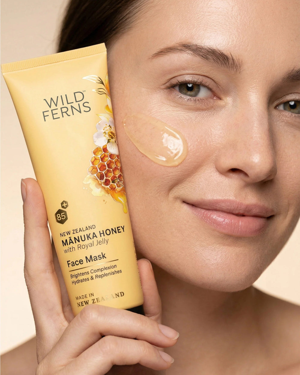 Woman holding a Wild Ferns Manuka Honey Face Mask with visible honeycomb design on a beige background