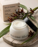 Wild Ferns facial cleansing balm jar with packaging and leaves on a wooden board