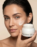 Woman applying facial cream to her face with a jar of Wild Ferns product.