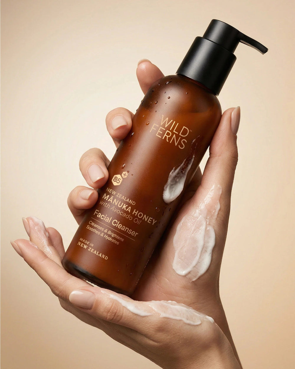 Hand holding a bottle of Wild Ferns facial cleanser with a beige background