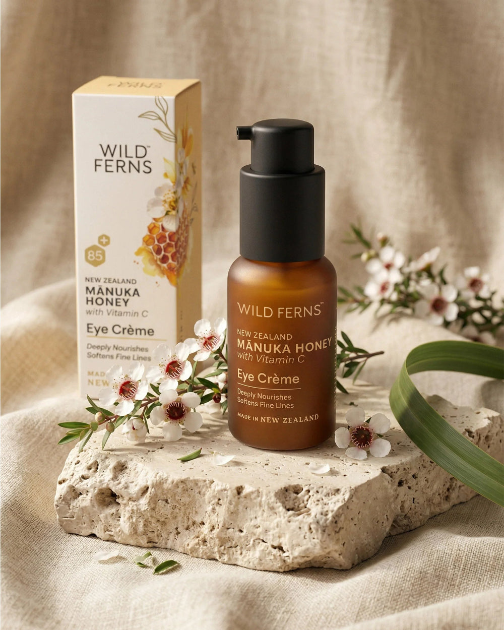 Wild Ferns Manuka Honey Eye Crème bottle and packaging on a stone surface with flowers.
