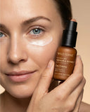 Woman holding a bottle of Wild Ferns Manuka Honey Eye Crème near her face.