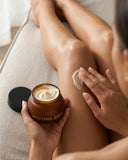 Person applying cream to their leg with a jar of Wild Ferns cream in hand.