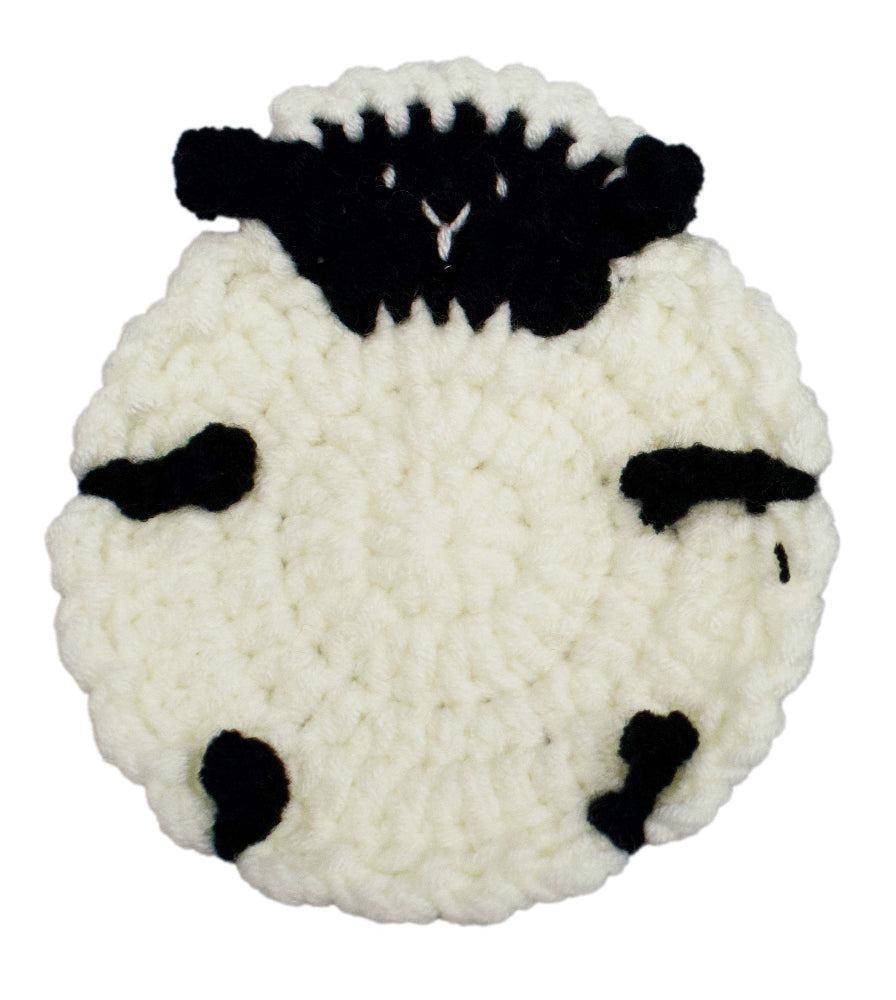 A round, hand-crocheted sheep-shaped item, likely a coaster or decorative mat, featuring a textured off-white body with black yarn details for the face, ears, and markings.