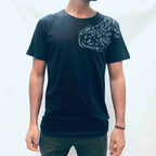 A man wearing a black crew neck T-shirt with a Maori shoulder tattoo design printed on the front.