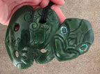Green jade pendant with intricate carvings held in a hand on a beige surface