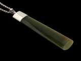 A polished green jade pendant necklace with a silver-toned metal cap and chain, shown against a solid black background.