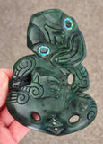 Green jade pendant with intricate carvings held by a hand on a neutral background