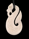 Carved bone pendant with intricate patterns on a black background