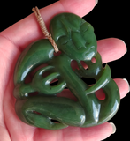 A carved green jade-like pendant with a coiled snake design and a small loop at the top, held in a person's hand against a black background.