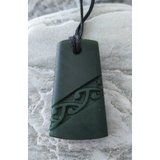 Green jade pendant with intricate carvings on a sandy background