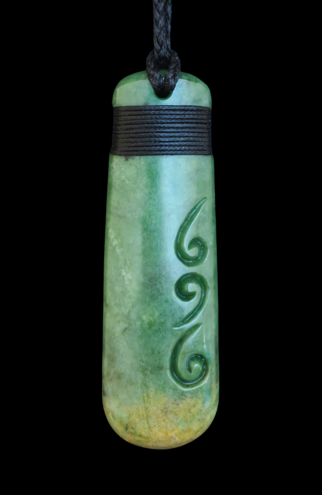 Greenstone pendant with spiral design on a black background