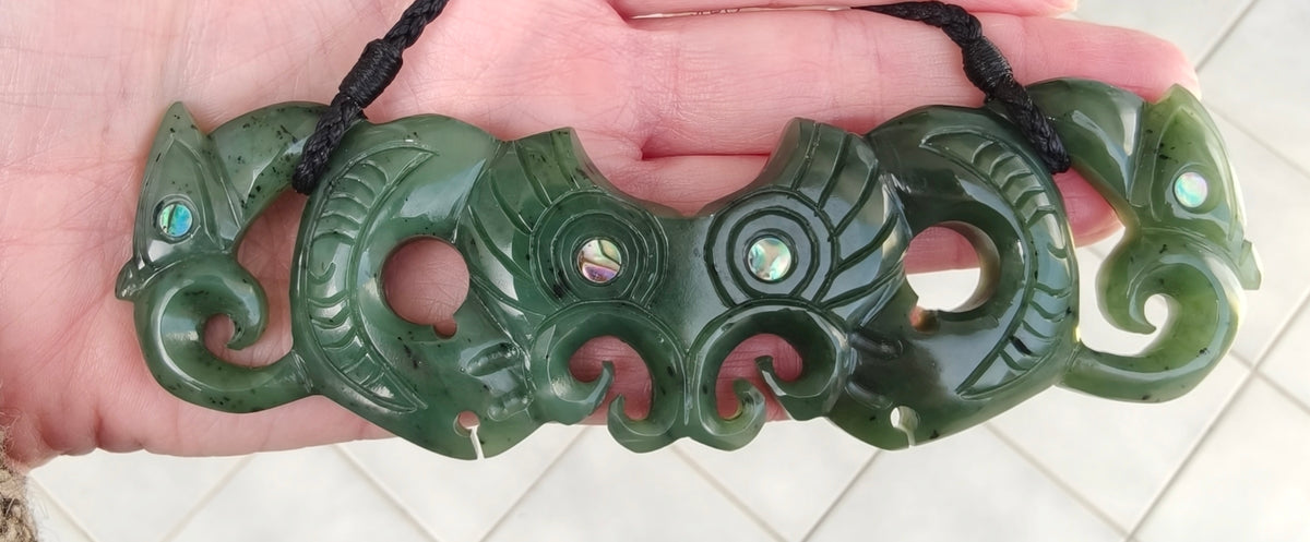 Green jade necklace with fish design held in a hand on a white tiled floor.